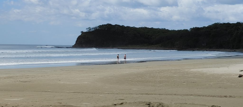 Photo of a sandy beach with two people walking by the shore.