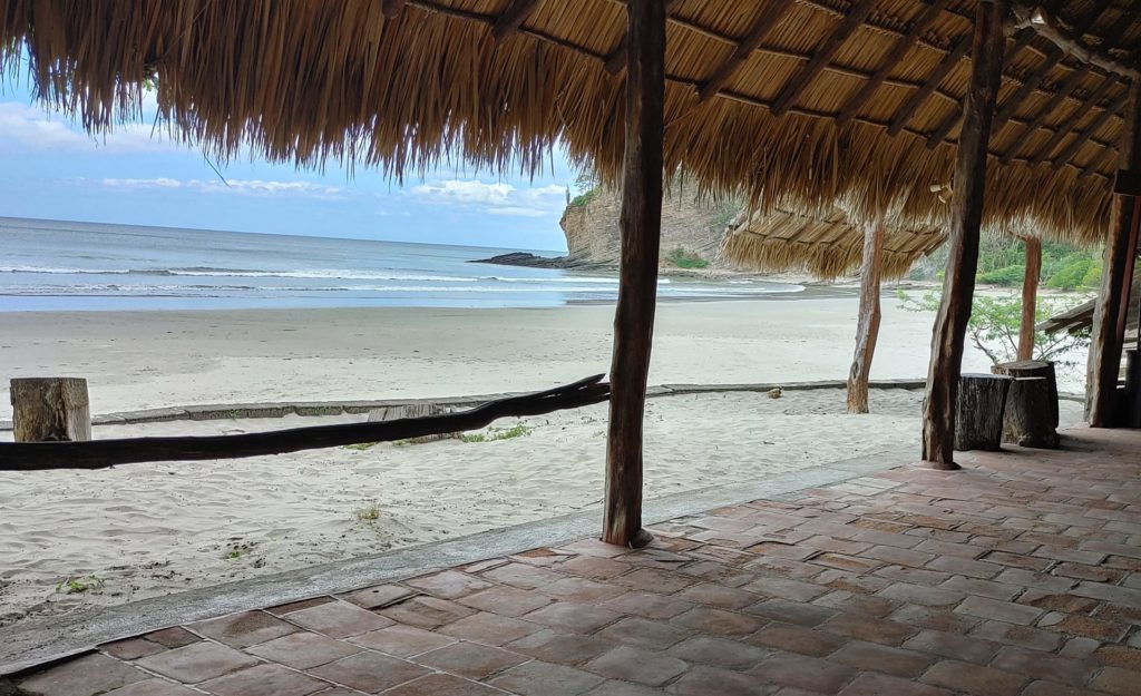 Photo of beach taken under palm leaf roof.