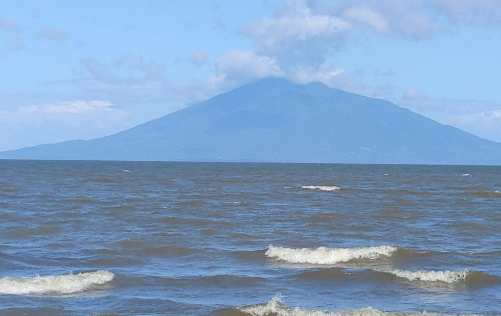 Beach with waves, tall mountain in the distance.