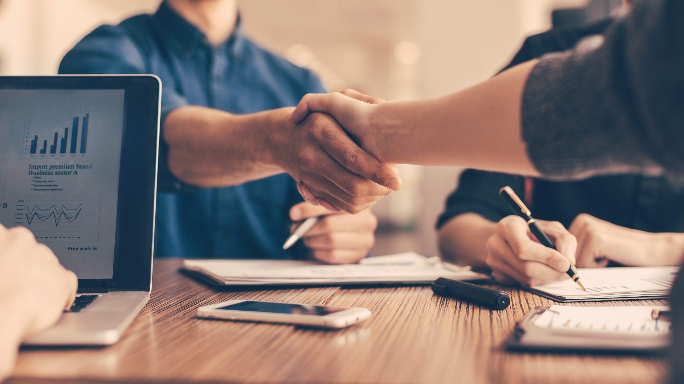 Close up of people shaking hands at a work table.